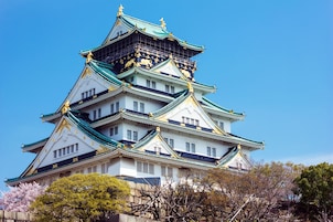 A traditional Japanese castle with multiple tiers, white walls, and green and gold roofs.