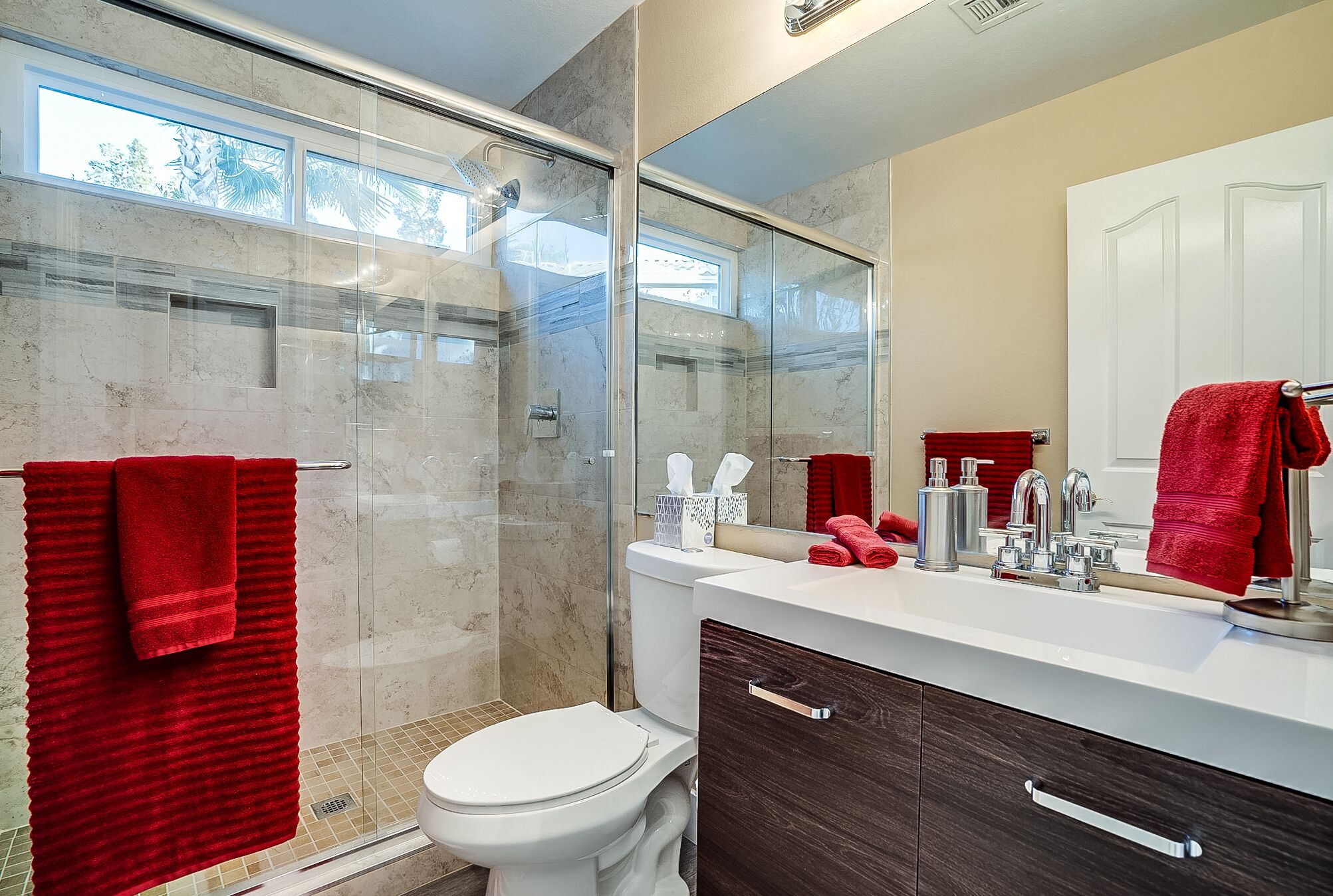 A modern bathroom with a glass-enclosed shower, a white toilet, and a vanity with dark wood cabinets.