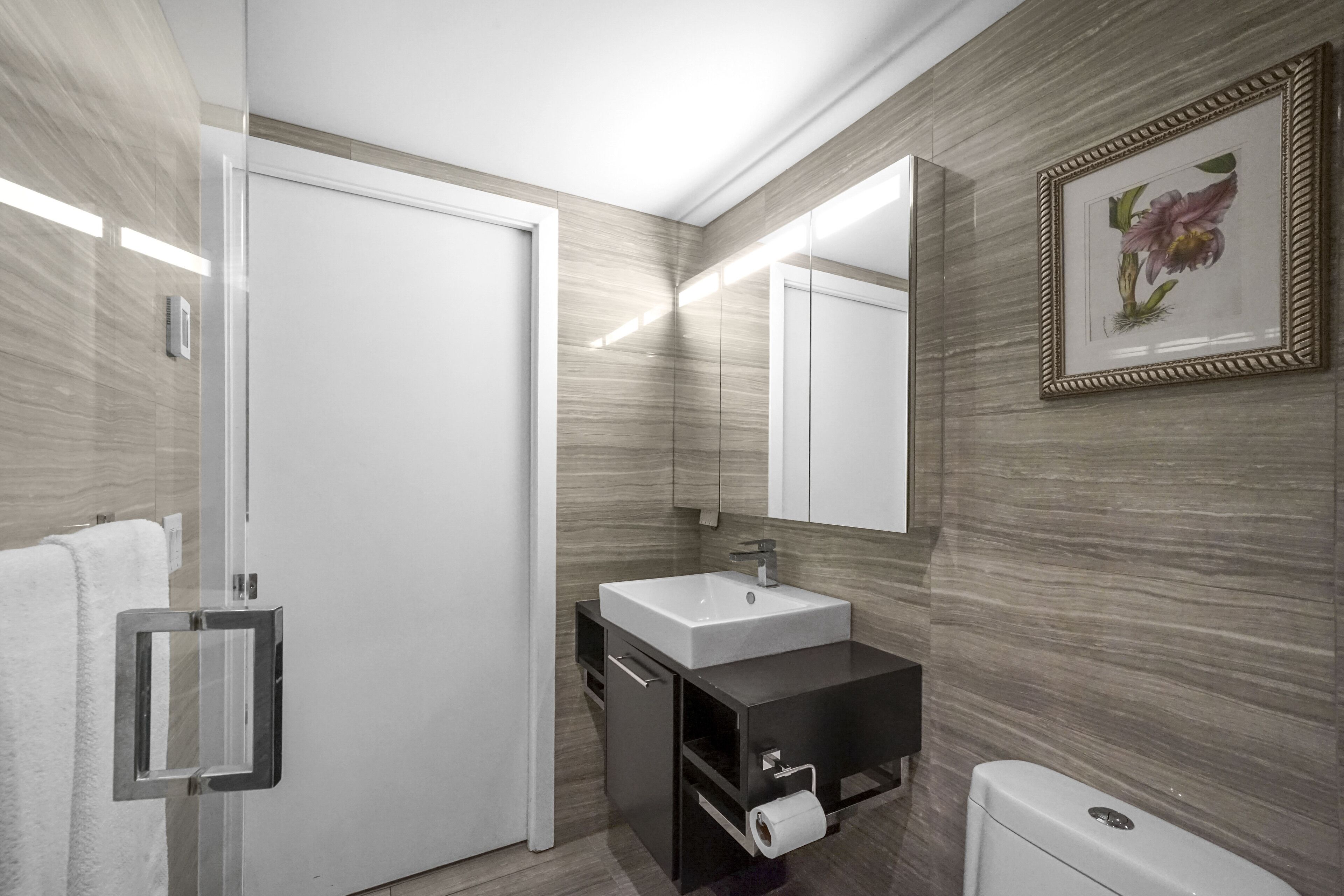 Un baño moderno con un lavamanos blanco, tocador oscuro y un inodoro.