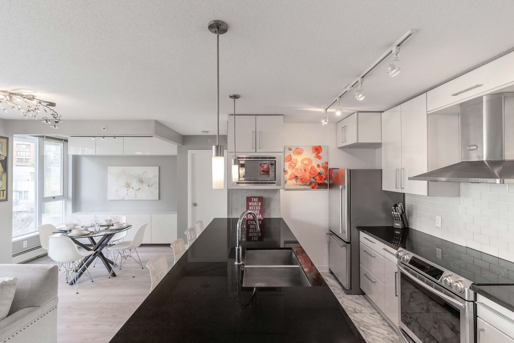 A modern kitchen with white cabinetry, a black countertop, and stainless steel appliances.