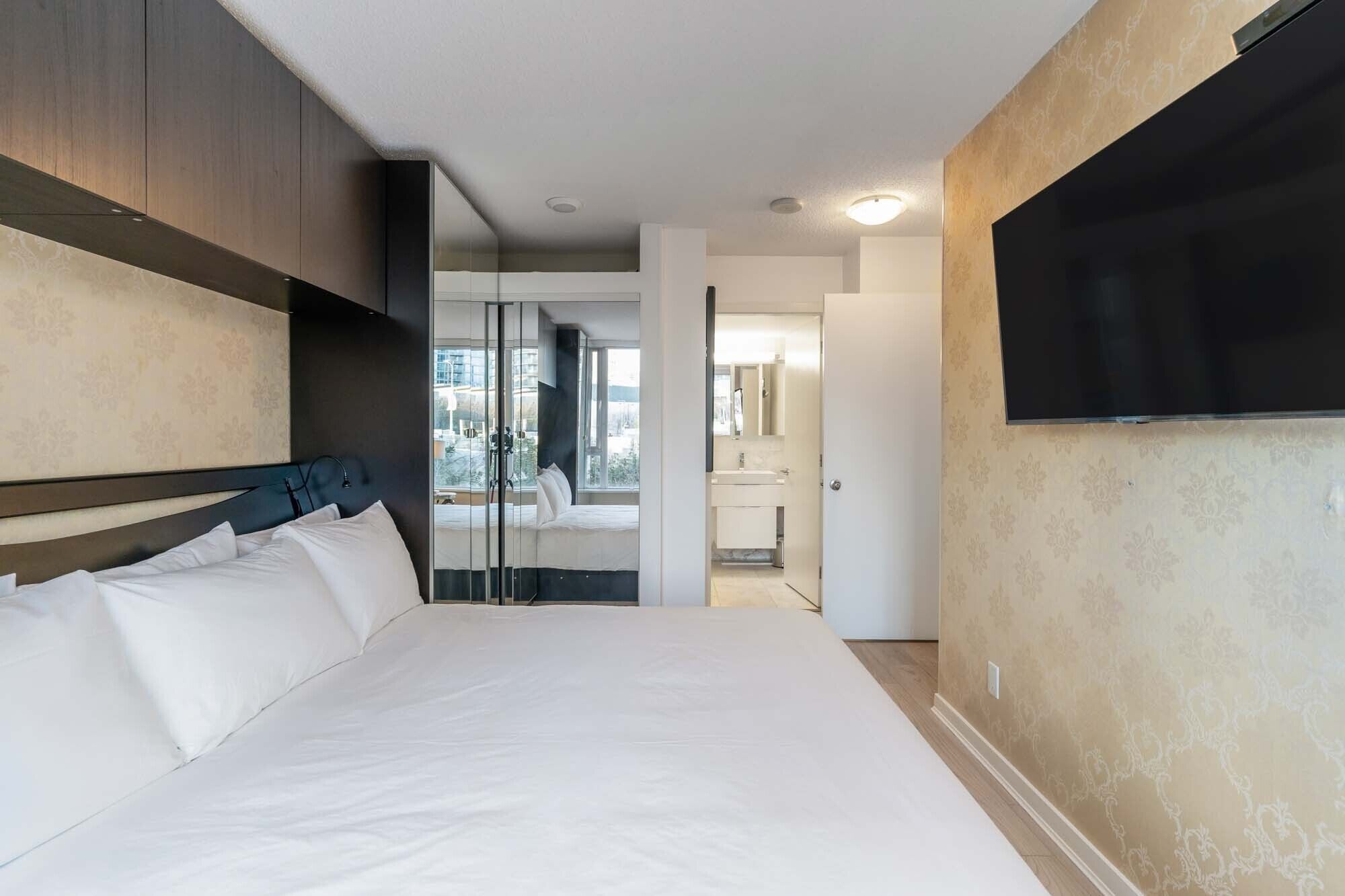A hotel room with a large bed, a TV mounted on the wall, and a bathroom visible through a glass door.