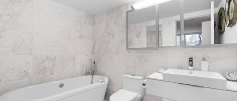 Un baño moderno con una bañera independiente, un inodoro y un tocador con espejo.