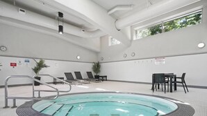 Een zwembad met een jacuzzi, ligbedden en een tafel met stoelen.