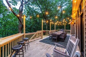 Una terraza de madera con una mesa y sillas, rodeada de árboles y luces colgantes.
