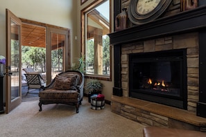 Cozy space with a fireplace, comfortable armchair, and dining area through large windows.