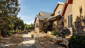 A residential building with a stone facade, a metal roof, and a landscaped garden with rocks and shrubs. - Zion (East) Luxurious Home King Beds WiFi Privacy Hot Tub (Orderville)
