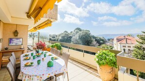 A balcony with a table set for dining, surrounded by wicker chairs, and overlooking a scenic view of trees and buildings. - LE CHATEAU DE LA PINEDE AP4198 (Juan-les-Pins)