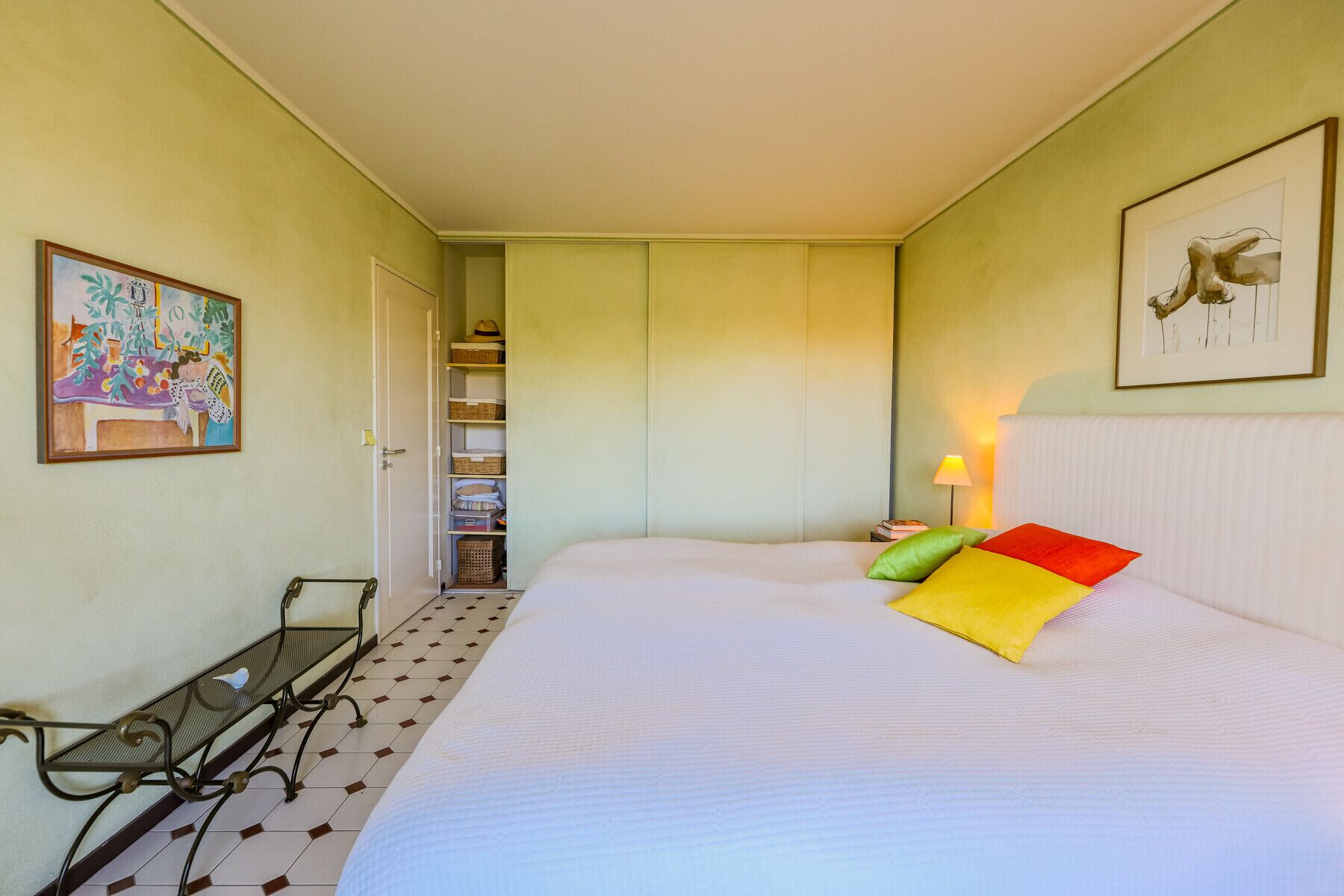 Een slaapkamer met een bed, een nachtkastje, een stoel, een plank met manden, en een deur naar een inloopkast.