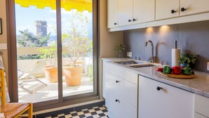 A kitchen with a sink, cabinets, and a view of a balcony with potted plants and a chair. - LE CHATEAU DE LA PINEDE AP4198 (Juan-les-Pins)