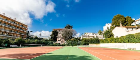 Una cancha de tenis con red, rodeada de edificios y árboles.