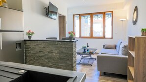 A modern kitchen with a stone island, a dining area with a table and chairs, a sofa, and a large window with a view of buildings. - MASSENET PIETONNE  AP4196 by Riviera Holiday Homes (Niza)