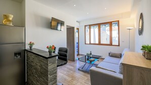 A modern kitchen with a built-in refrigerator, a stone accent wall, a flat-screen TV, and a dining area with a glass table and a sofa. - MASSENET PIETONNE  AP4196 by Riviera Holiday Homes (Niza)