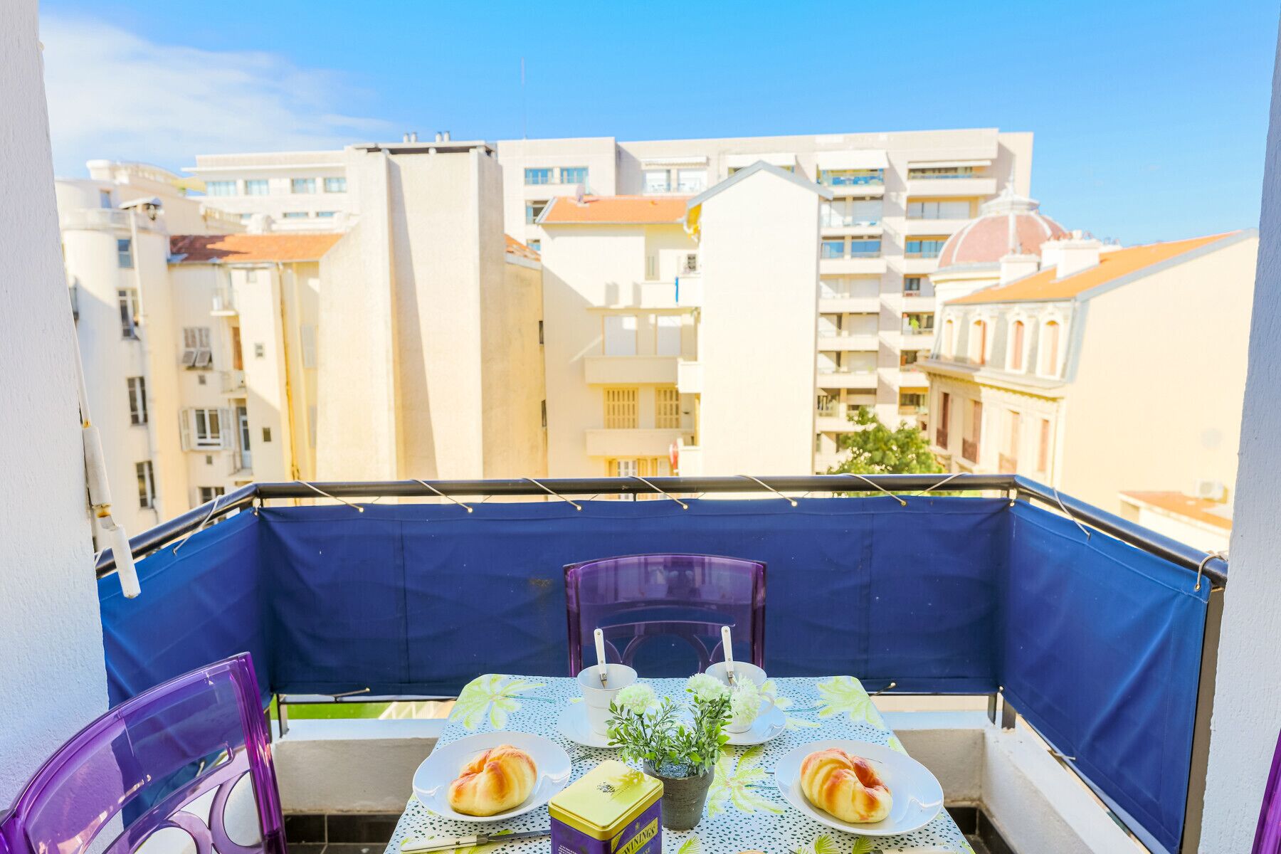 A balcony with a table set for two, two chairs, and a small potted plant.