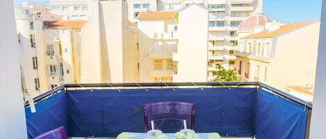 A balcony with a table set for two, two chairs, and a small potted plant.