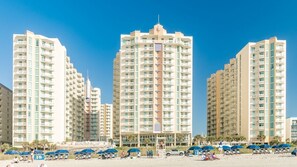 A beachfront hotel with multiple high-rise buildings, beach umbrellas, and a clear blue sky.