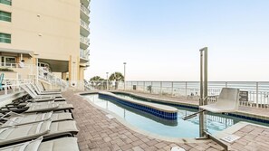 A pool area with lounge chairs, a pool, and a view of the beach.