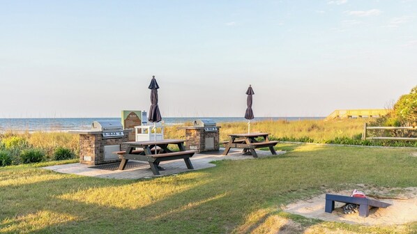 An outdoor patio with two picnic tables, a grill station, and a view of the ocean.