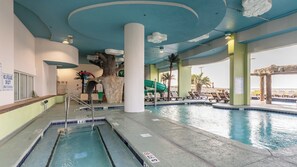 Una piscina interior con cascada, sillas de descanso y decoración tropical.