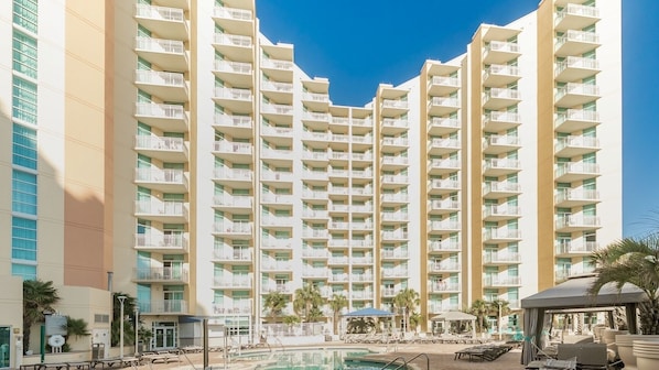 Un hotel de altura con varios balcones, piscina y palmeras.