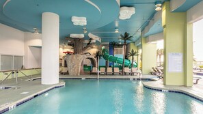 Une piscine intérieure avec un toboggan, des chaises longues et un panneau indiquant les règles de la piscine.
