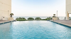 A swimming pool with a view of the sea, surrounded by palm trees and a building with a balcony.