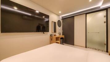 A modern hotel room with a large bed, a vanity with a mirror, a small desk, and a sliding door closet.