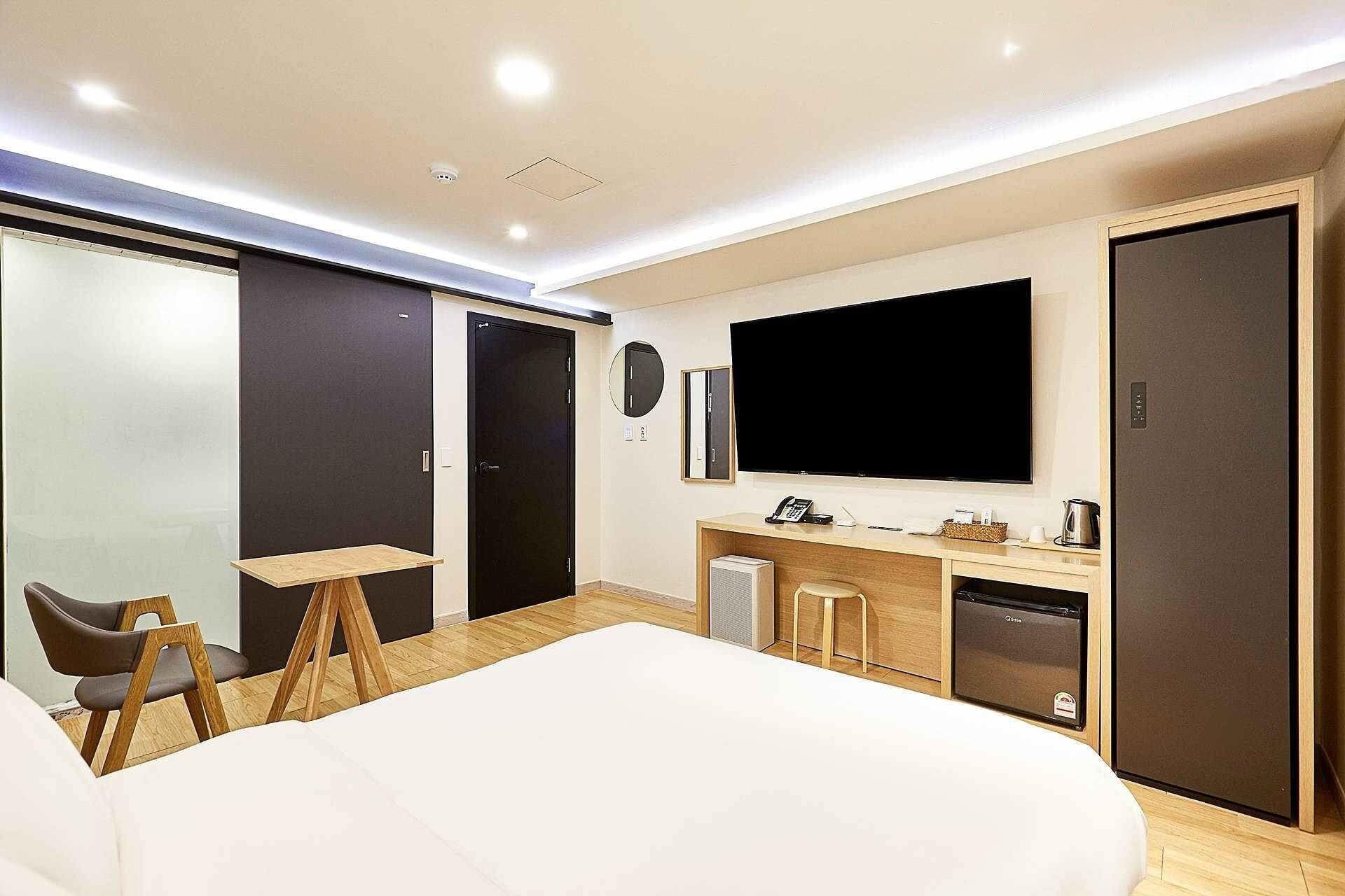 Una habitación de hotel moderna con una cama grande, un escritorio con computadora, un televisor de pantalla plana, un minibar y un armario.