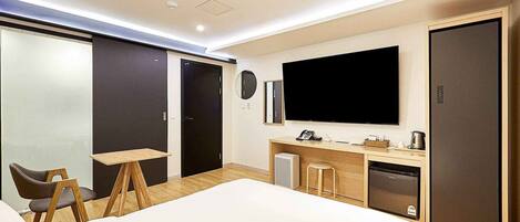 Una habitación de hotel moderna con una cama grande, un escritorio con computadora, un televisor de pantalla plana, un minibar y un armario.