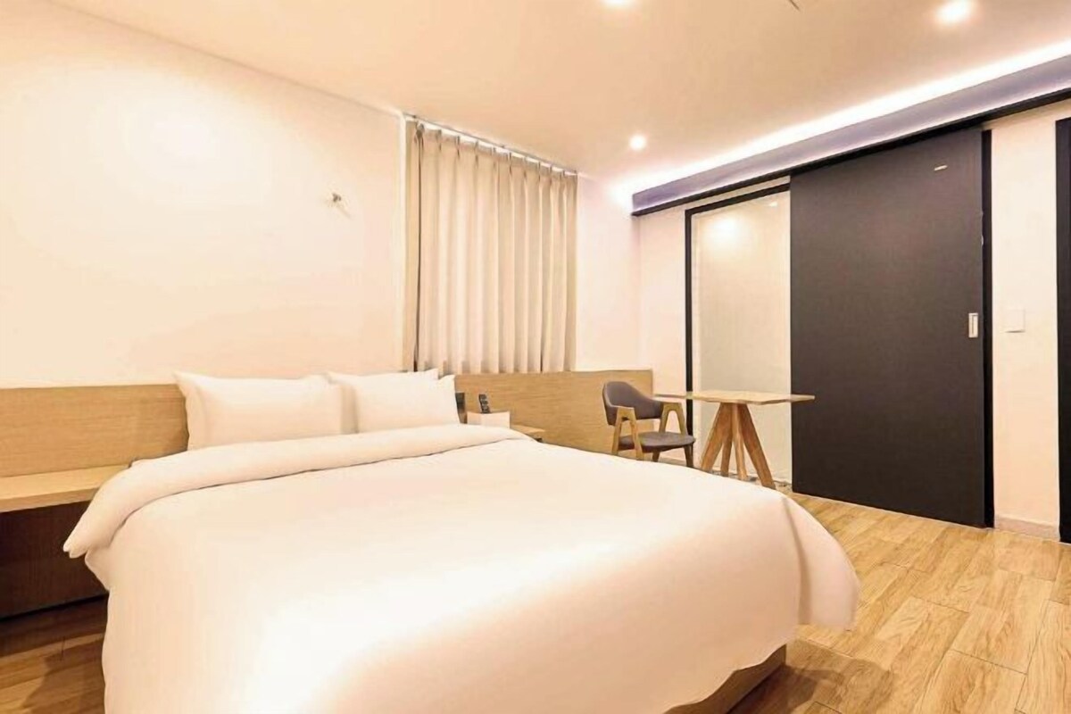 A modern hotel room with a large bed, a desk, and a sliding door.