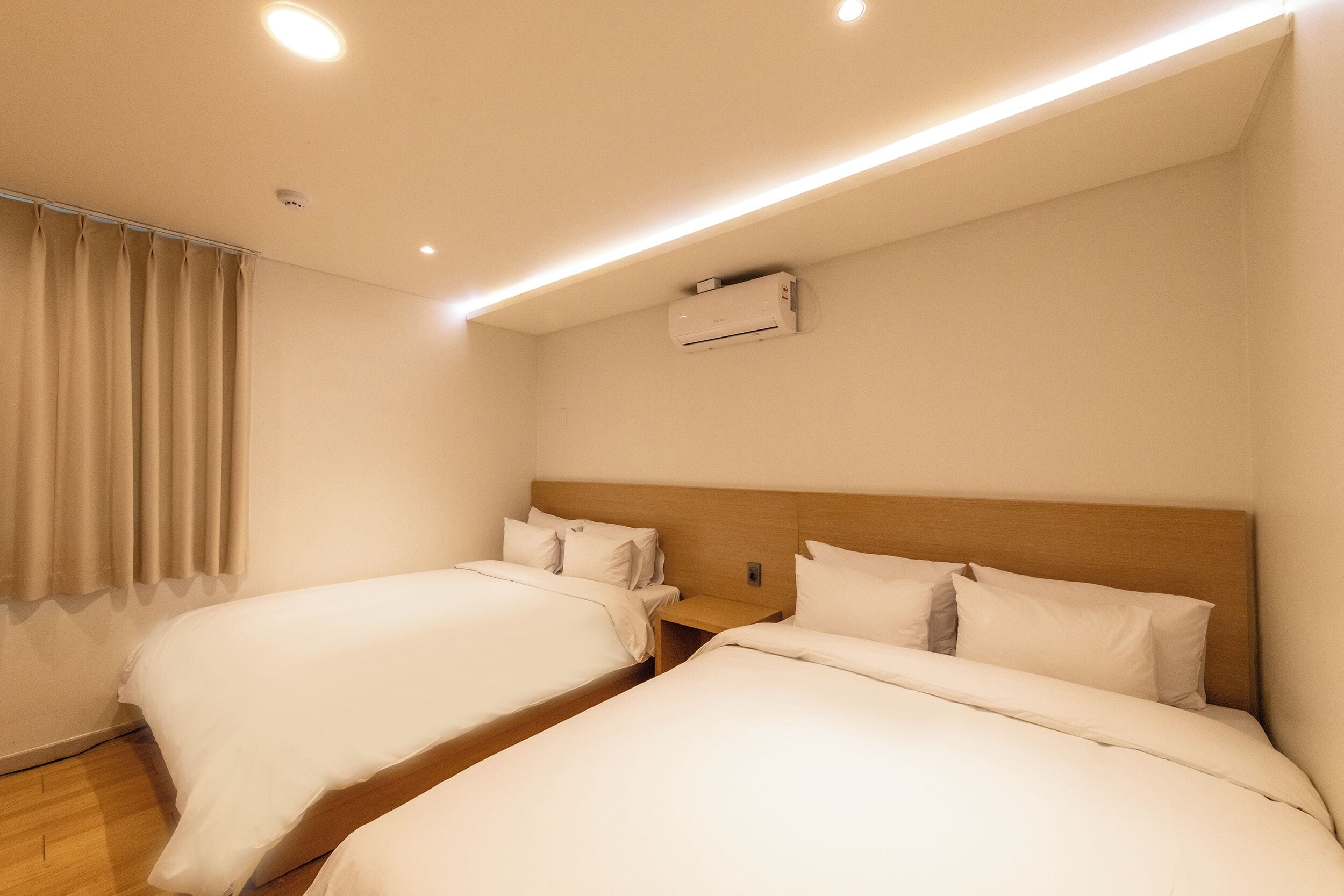A hotel room with two single beds, a wooden headboard, a nightstand, and an air conditioning unit.