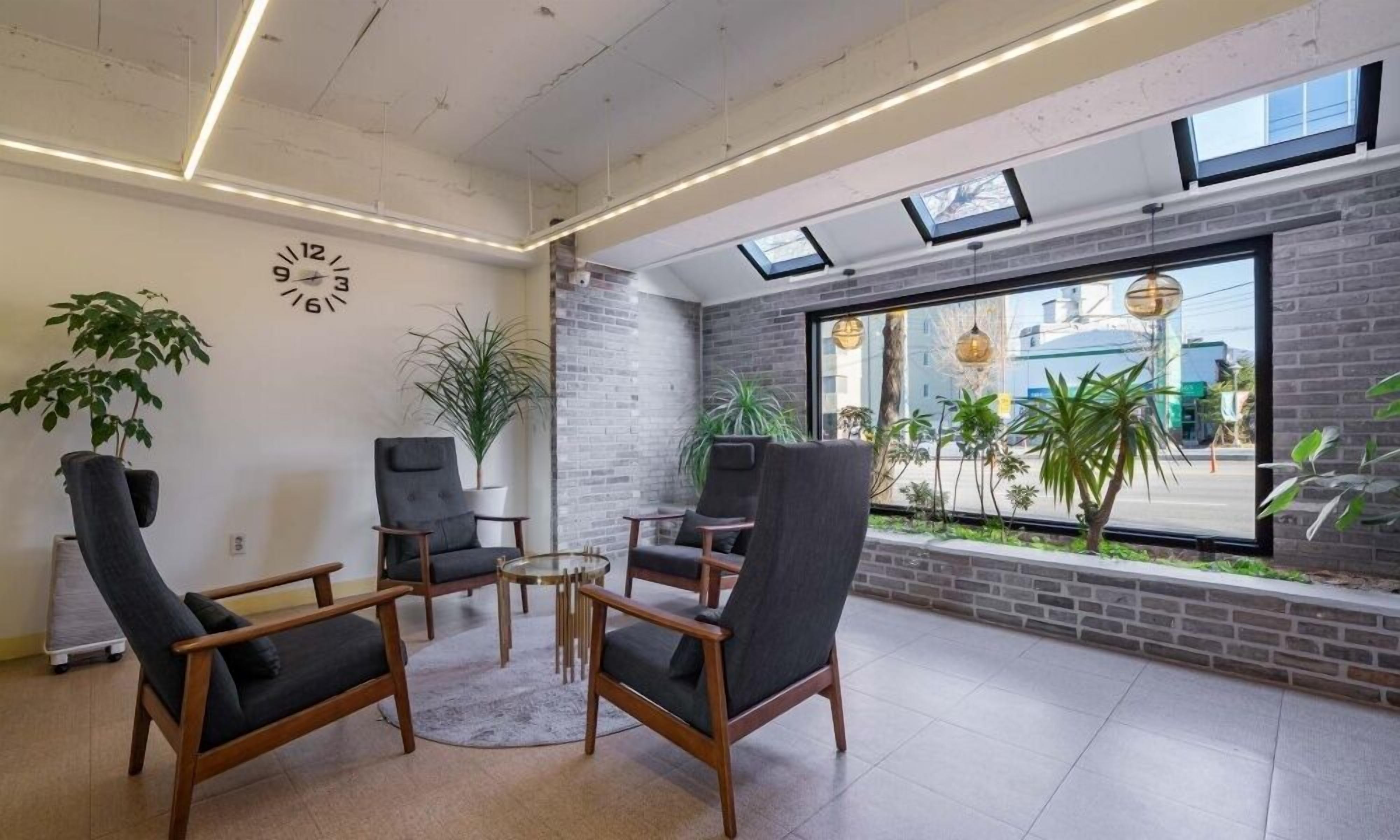 Un área de espera moderna con sillones de cuero, una mesa redonda y plantas en macetas.