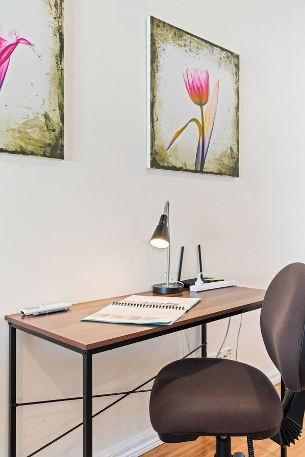 Un espace de travail comprenant un bureau, une chaise, une lampe et deux œuvres d’art encadrées accrochées au mur.
