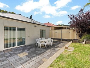 Il s’agit d’une propriété résidentielle dotée d’un patio comprenant une table et des chaises, une porte-fenêtre coulissante et un jardin clôturé.