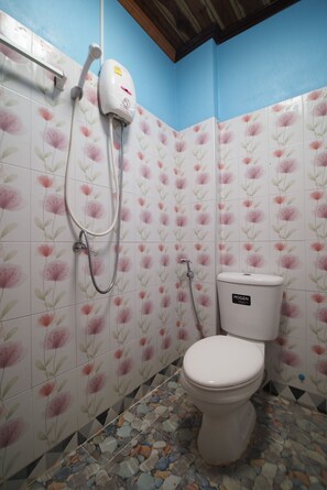 A bathroom with floral-patterned tiles, a toilet, and a shower with a hose.