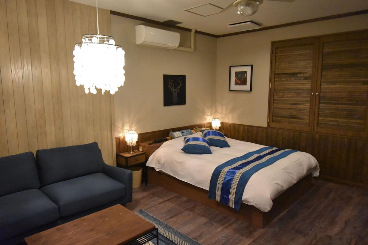 A bedroom with a bed, a sofa, a nightstand, a lamp, and a ceiling fan.