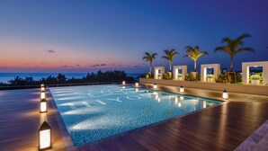 Une piscine sur le toit, avec une terrasse en bois, des palmiers et une vue sur la mer au crépuscule.