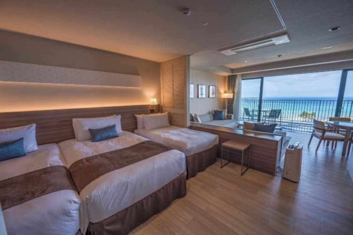 Une chambre d’hôtel avec trois lits, un balcon et vue sur la mer.