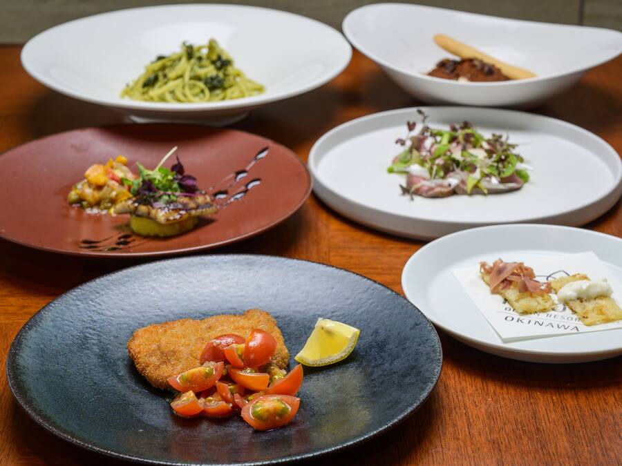 A variety of dishes on plates, including pasta, a salad, and a fish dish, arranged on a wooden table.