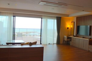 Una habitación de hotel moderna con un balcón grande, un televisor de pantalla plana, un escritorio y una zona de estar cómoda.