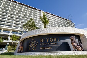 Señal de Hiyori Ocean Resort en Okinawa, con una estatua de león y un edificio al fondo.