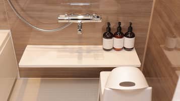 A modern bathroom with a shower, a white sink, and three bottles of shampoo and conditioner on the sink.