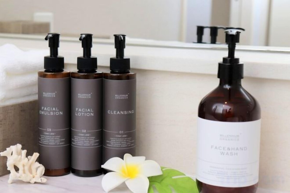 A bathroom with a sink, three bottles of facial products, and a large bottle of face and hand wash.