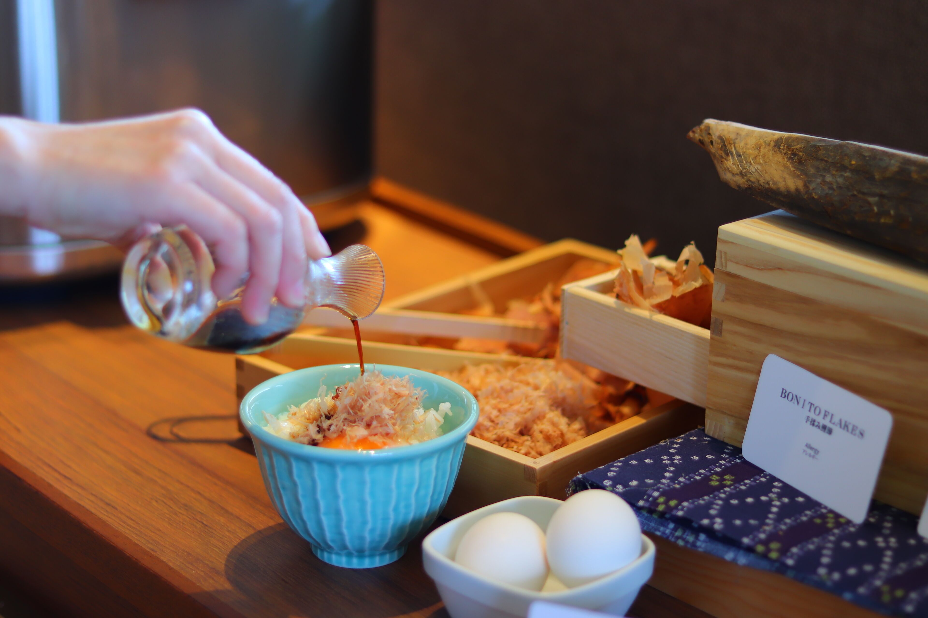 Ein Holztisch mit einer blauen Schüssel mit einer Mischung, einer weißen Schüssel mit Eiern und einer Holzkiste mit dem Aufdruck "BON TO FLAKES".