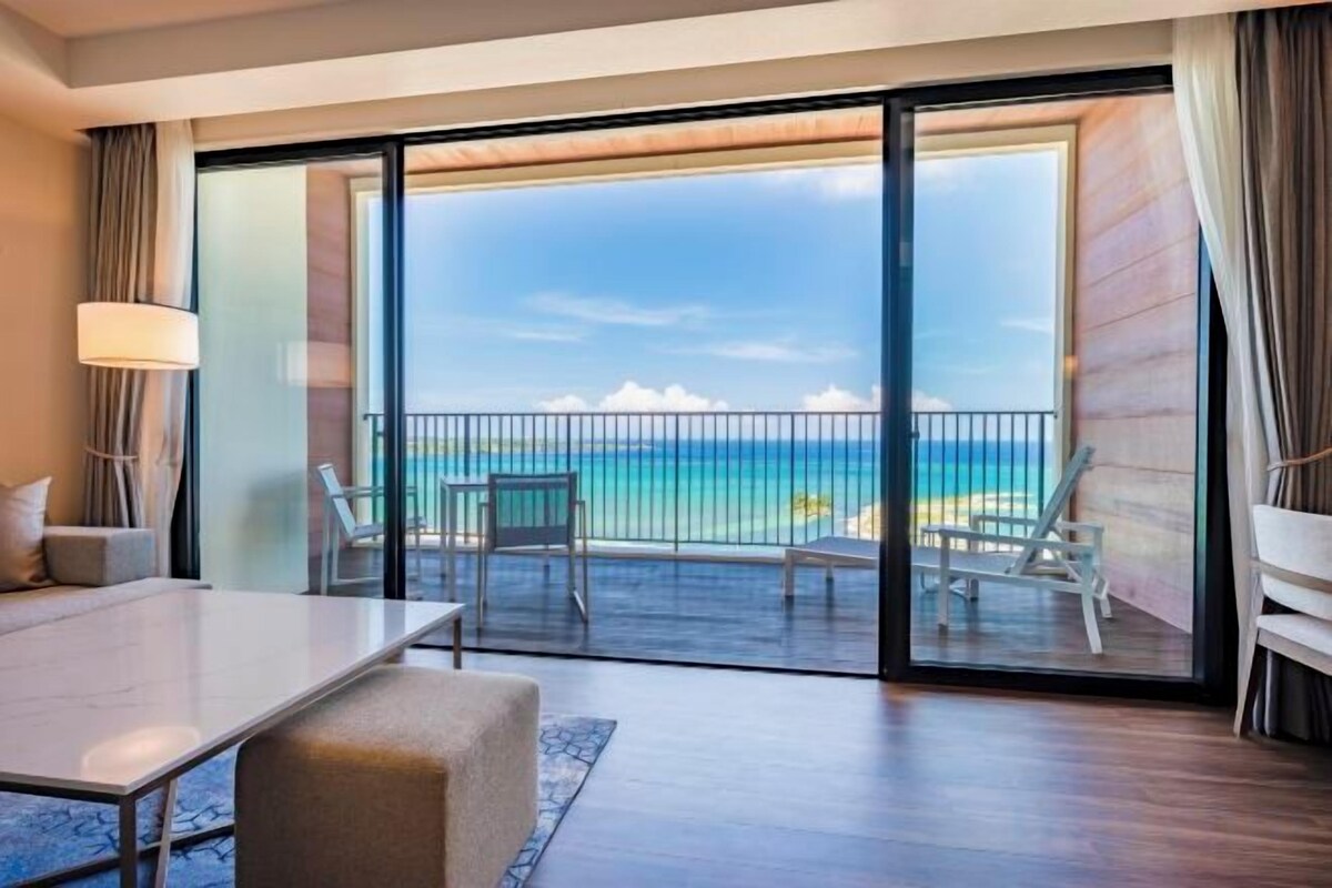 A hotel room with a balcony, a bed, a table, and a view of the ocean.