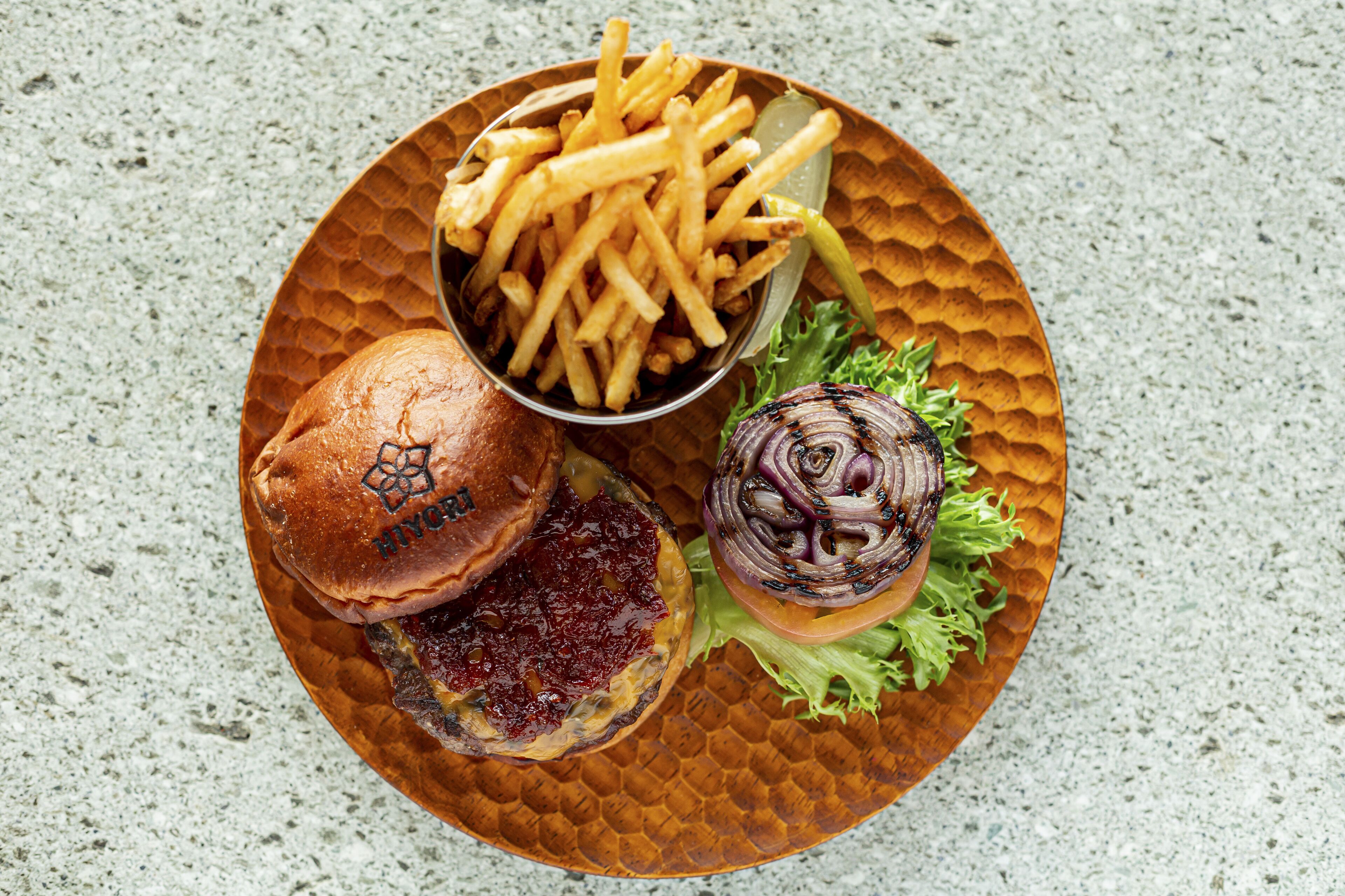 A meal consisting of a burger, fries, and a grilled onion on a textured plate.