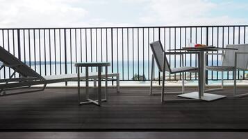 A balcony with a view of the sea, featuring a table, chairs, and a lounge chair.