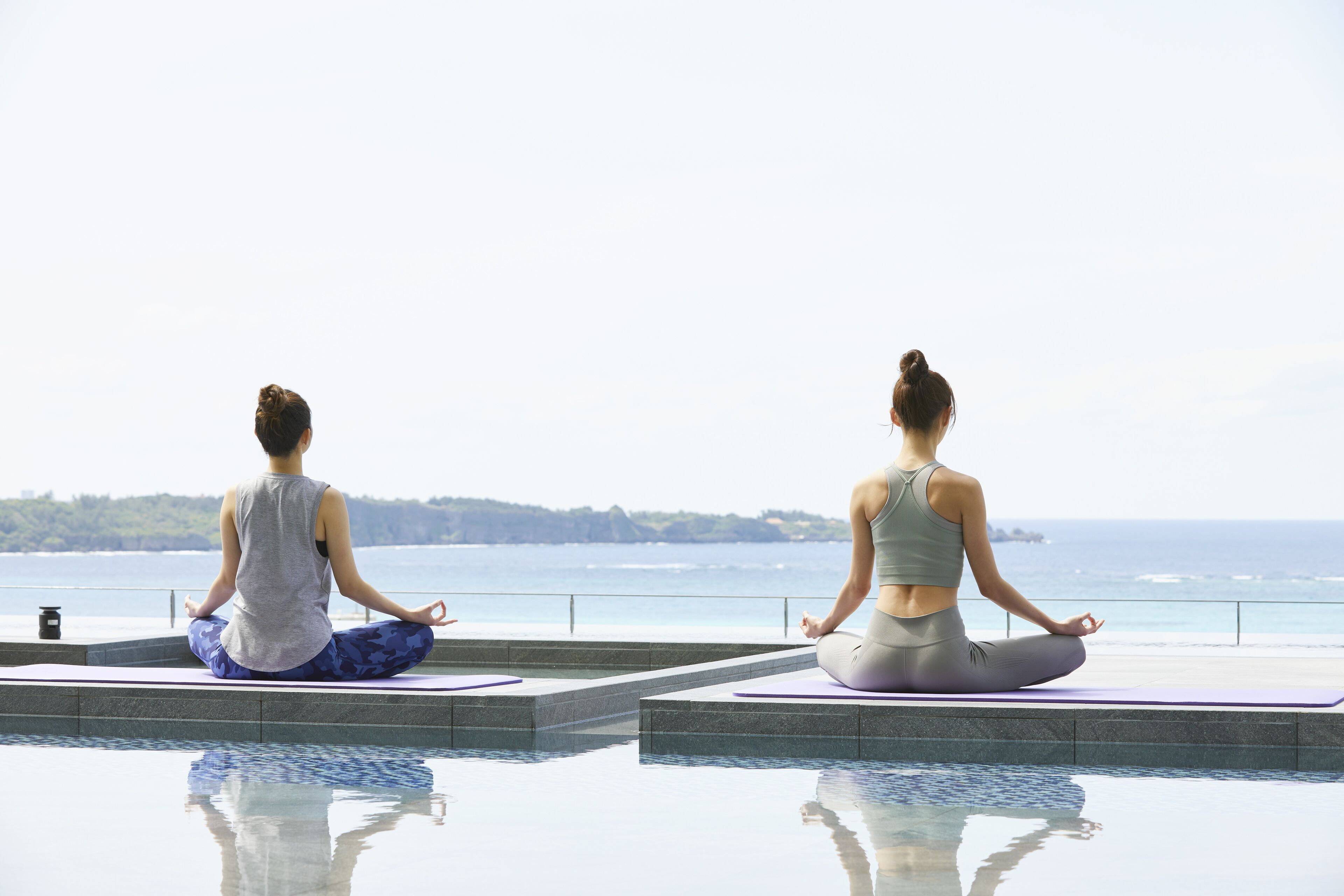 Two individuals meditating on a balcony with a view of the ocean.