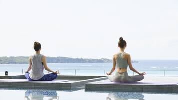 Two individuals meditating on a balcony with a view of the ocean.