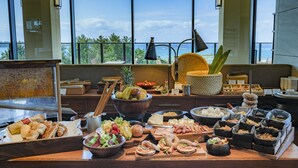 Une table de buffet garnie de divers plats et une grande fenêtre donnant sur l’océan.