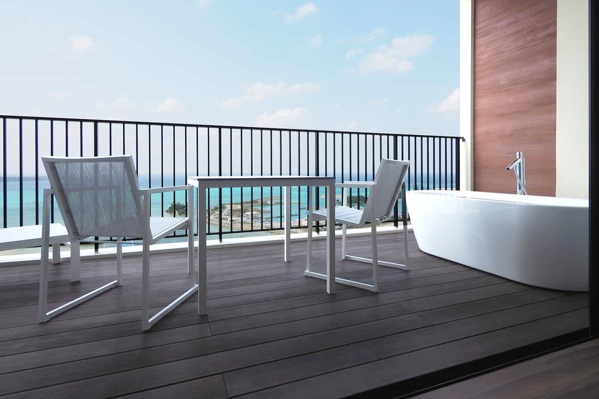 Un balcon avec deux chaises blanches et une table blanche, d’où l’on peut admirer un plan d’eau et une côte lointaine.